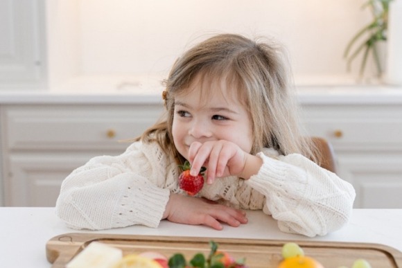 Child eating a strawberry at a kitchen counter